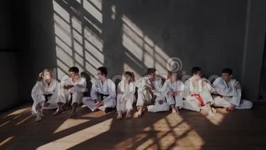 跆拳道学校的青少年在经过紧张的武术训练后放松。 他们白坐在墙边聊天